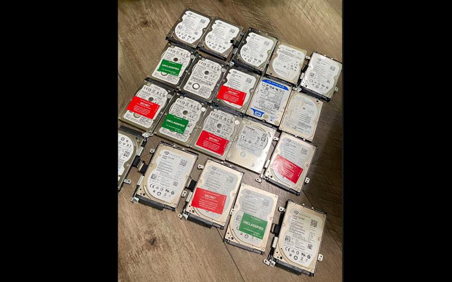 Overhead view of 20 computer hard drives, arranged in rows on a brown tabletop.