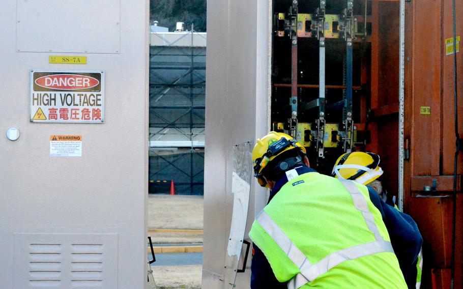 Workers wearing yellow safety gear attempt to fix electrical issues in an area marked “danger high voltage.”