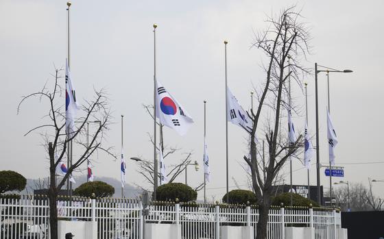 South Korean flags fly a half-staff above a fence outside a government building.