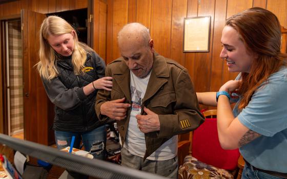 Kayla Smith, left, and Hannah Winton help Andy Valero try on an Eisenhower jacket from the World War II era at his Virginia home. MUST CREDIT: Kyle Cummings/Randolph-Macon College