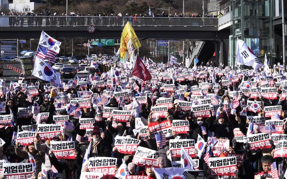 A large group of South Korean protesters waves signs and flags.