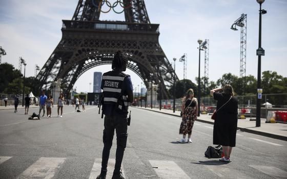FILE - A security officer watches people taking photographs in front of the Eiffel Tower ahead of the 2024 Summer Olympics, Saturday, July 20, 2024, in Paris, France. Three days before the start of the Olympics, France's Interior Minister has hailed the country’s law enforcement for their hard work in making the Paris Games safe for 10,500 athletes and millions of visitors. (AP Photo/Thomas Padilla, File)
