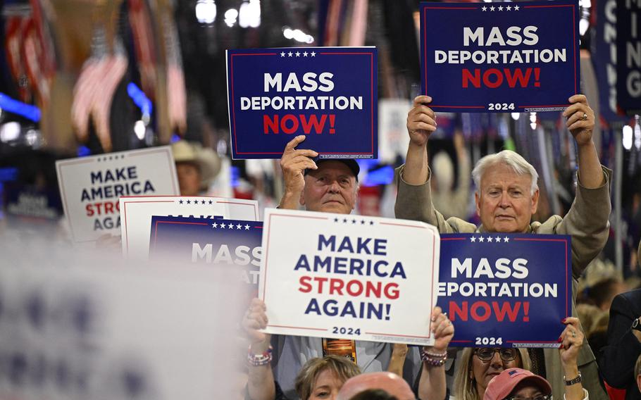 People at the Republican convention hold up signs that say Mass Deportation NOw! and Make America Strong Again!