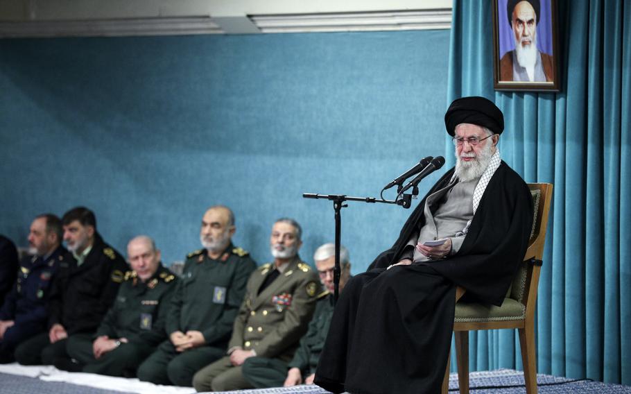 Ali Khamenei sits in a chair, in front of a microphone, with military commanders seated behind him and to his left/