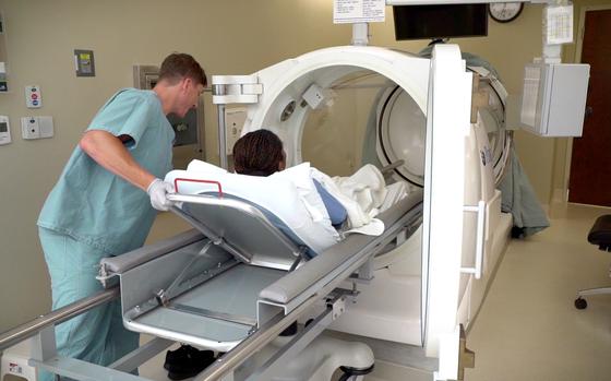 A staff member places a patient into the single hyperbaric oxygen chamber at the Undersea & Hyperbaric Medicine Clinic at Brooke Army Medical Center. Hyperbaric oxygen is an intervention in which an individual breathes nearly 100 percent oxygen while inside a hyperbaric chamber that is pressurized to greater than sea level pressure. (U.S. Army photo by James Camillocci)