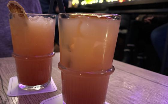 Two glasses with pink-colored mixed drinks sit on coasters on a table in a bar.