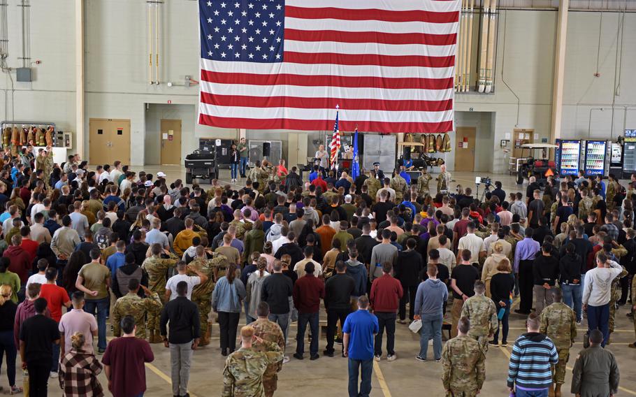 A group of people face a large American flag.