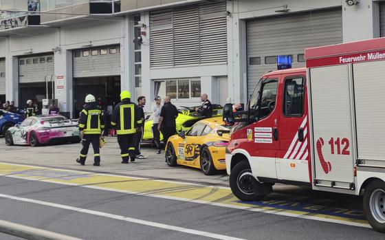 Firefighters walk in front of pit 27 in the pit lane of the Nuerburgring auto racing circuit, in Nuerburgring, Germany, on Friday, Aug. 2, 2024. Several people were injured during an accident allegedly caused by the explosion of a compressed air canister on Friday night in the paddock area of Germany's famous auto racing circuit Nuerburgring, German police said Saturday. (S'nke Brederlow/dpa via AP)