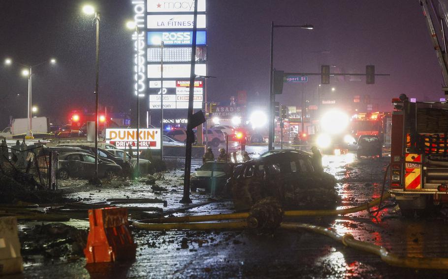 Lights from store billboards and emergency vehciles amid crash wreckage.