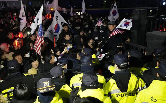 Korean protestors carrying American flags and South Korean flags attempt to breach a police barricade.