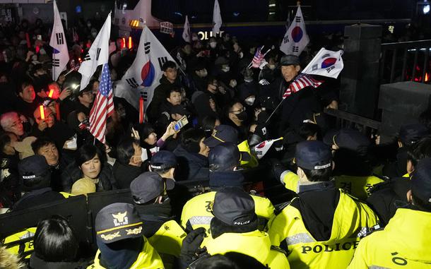 Korean protestors carrying American flags and South Korean flags attempt to breach a police barricade.