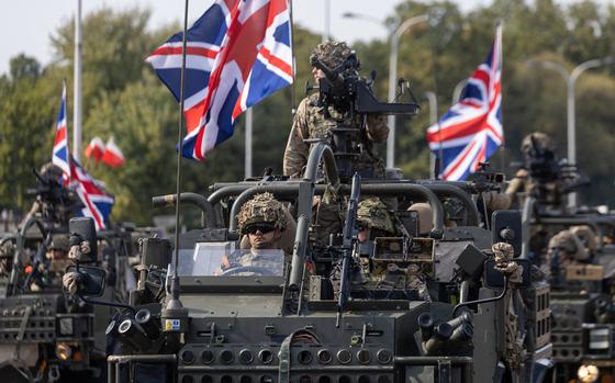 British soldiers ride armored vehicles, flags flying, during a parade.