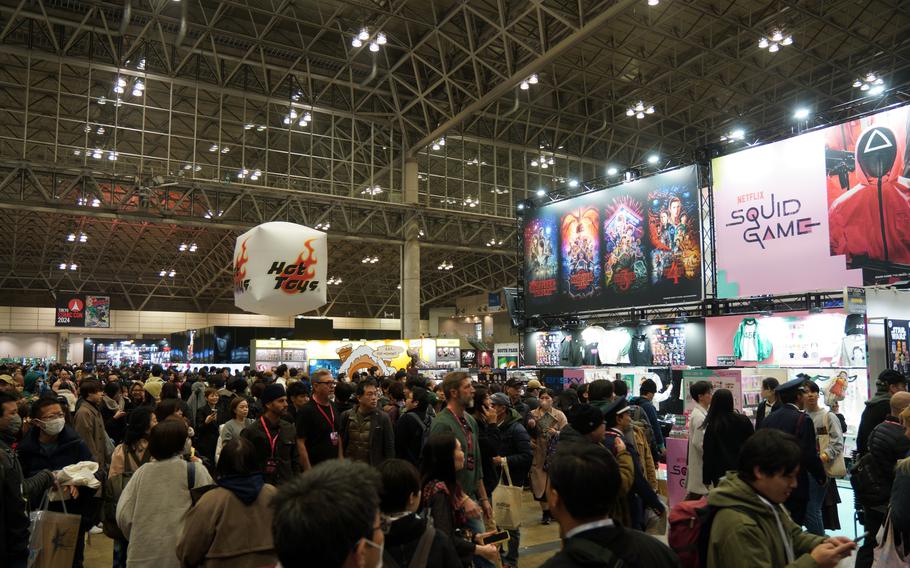 A crowd of people stand in a large convention center with movie and show advertisements above them.