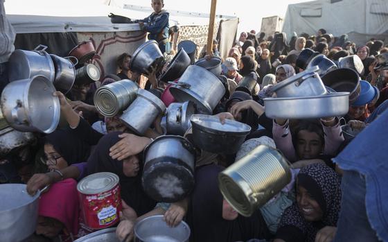 Palestinians extend pots and buckets outwards for food.