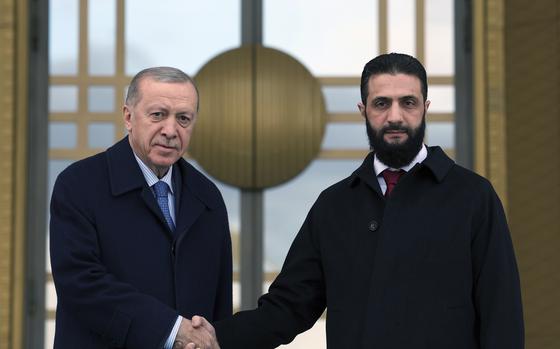 Two men shaking hands in front of a large window or door.