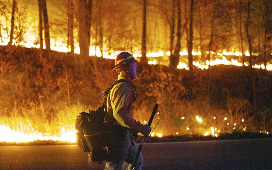 Flames burn in the background as a firefighter walks past in Jennings Creek, N.J.