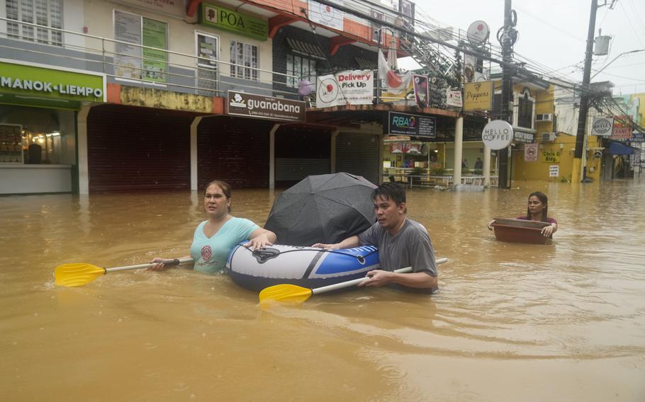 Residents use rubber paddles from a toy boat as they wade along a flooded street