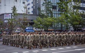 U.S. soldiers march down a street during a parade in Seoul, South Korea, past buildings and trees.