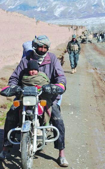 An Afghan familyon a motorcycle waits as U.S. soldiers change a flat tire on a Humvee that's blocking the way. 