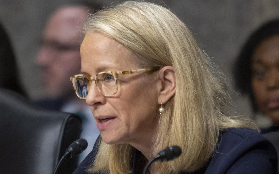 Morrison seated at a hearing speaking into a microphone.