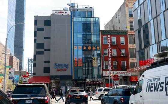 A line of three buildings in Manhattan’s Chinatown is seen, centered by an all-glass building with a blue tint.