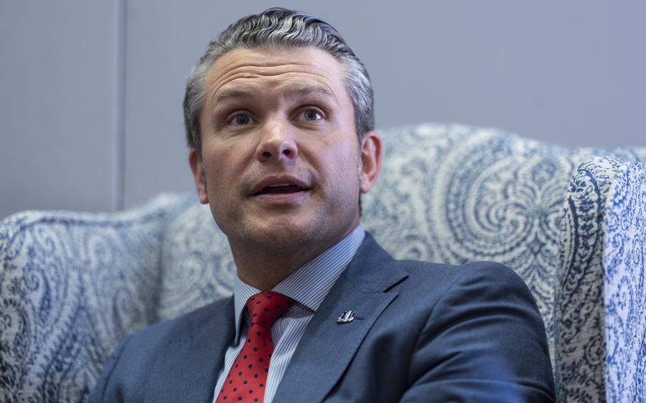 A man in a dark blue suit answers questions while seated in a chair.