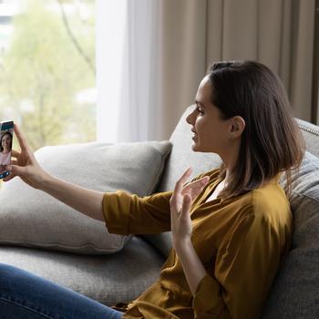 Concentrated young woman sitting on couch in living room, using smartphone, making video call,