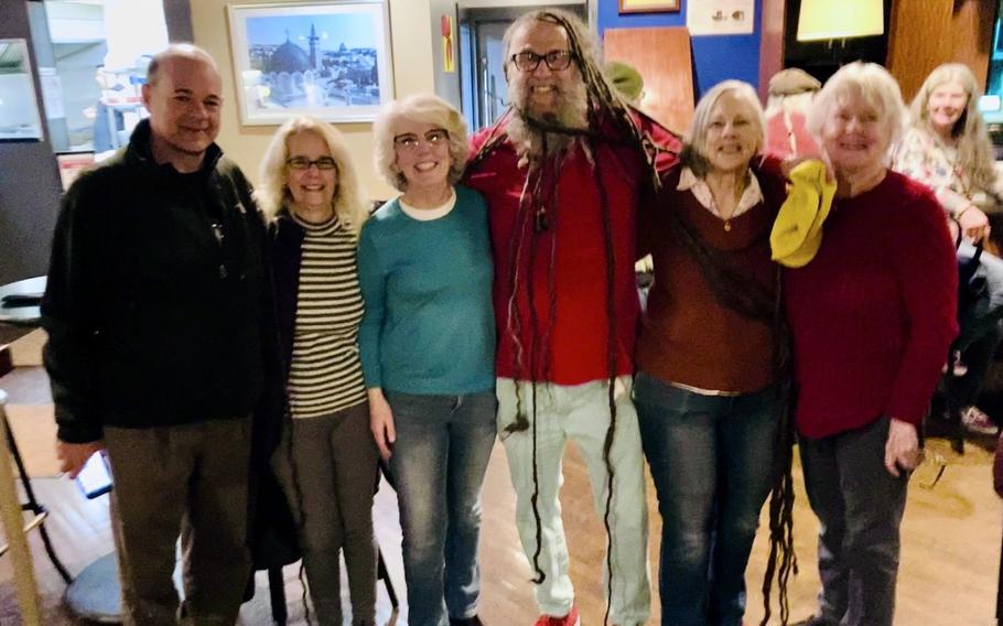 A man with very long dreadlocks stands in the center of a row of people posing for a photo.