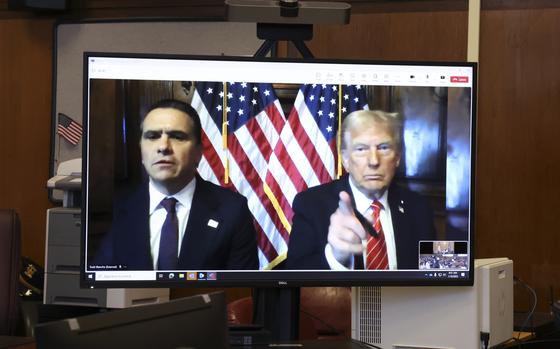 Donald Trump appears on the right side of a computer monitor that takes up the photo, pointing his index finger at the camera.