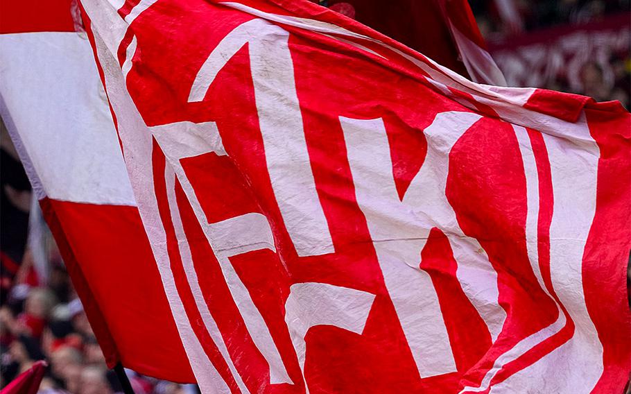 Red-and-white 1. FCK flags wave in a crowded stadium.