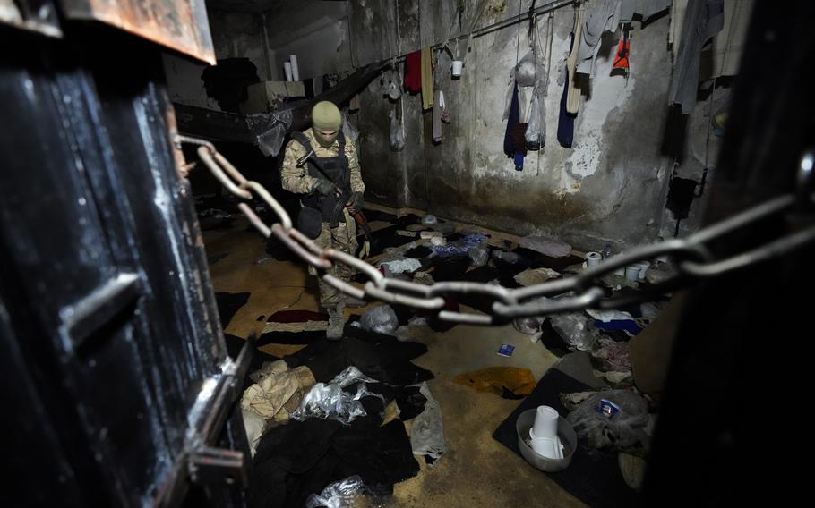 A soldier in combat gear inspects a prison cell.