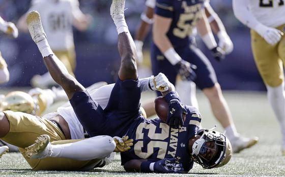 A Notre Dame football player tackles a Navy football player holding the football.