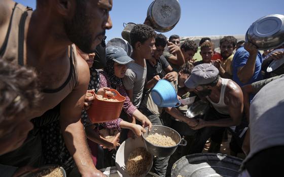 People hold out containers while waiting for food handouts at a refugee camp.