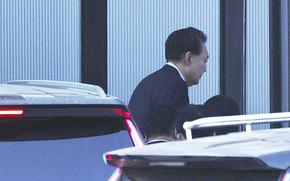 The South Korean president in a suit walks past vehicles and into a building.