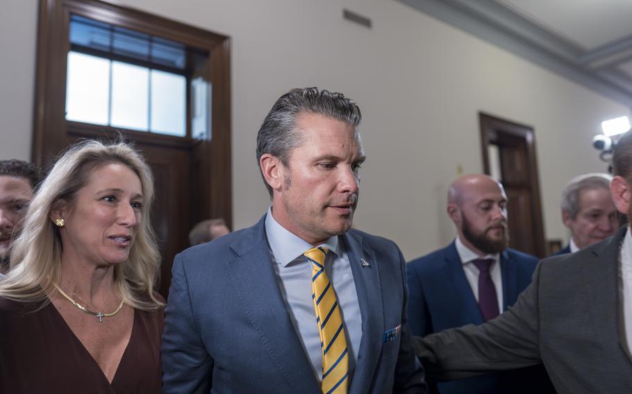 A gray haired man in a blue suit and yellow and blue striped tie walks next to a blonde woman.