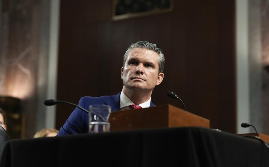 Pete Hegeth sits at a desk in front of a microphone.