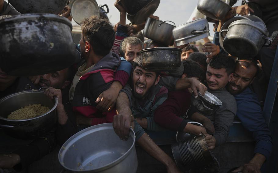 Men shout as they hold out metal pots for food.