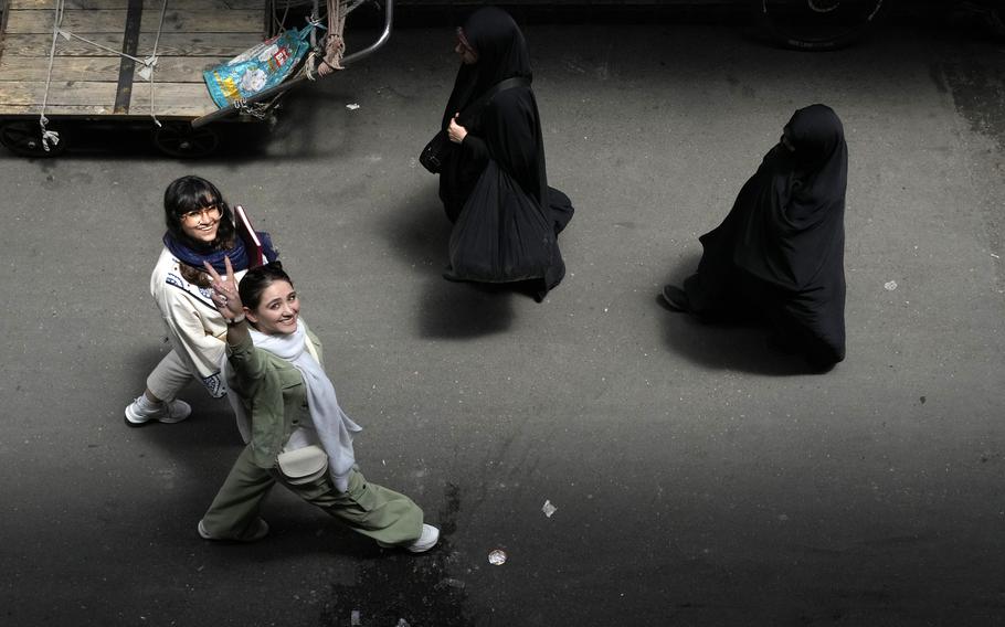 An Iranian woman without wearing her mandatory Islamic headscarf flashes a victory sign as two head-to-toe veiled women walk at the old main bazaar of Tehran, Iran.