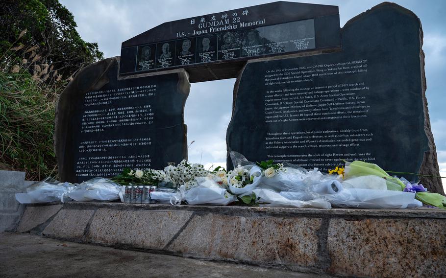 A monument composed of three large stones bears the images and names of fallen airmen who died in an Osprey crash, along with inscriptions in Japanese and English offering comfort to their spirits.