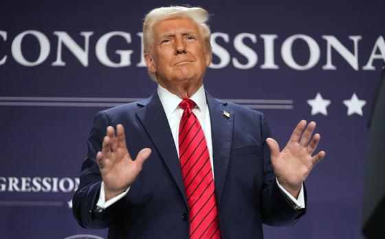 Donald Trump gestures with his hands outstretched while standing on a stage.