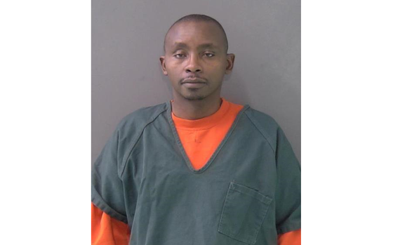 Mwangi in prison clothes standing for a mugshot.