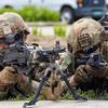 Two soldiers in combat gear lie on their stomachs and aim machine guns during an exercise.