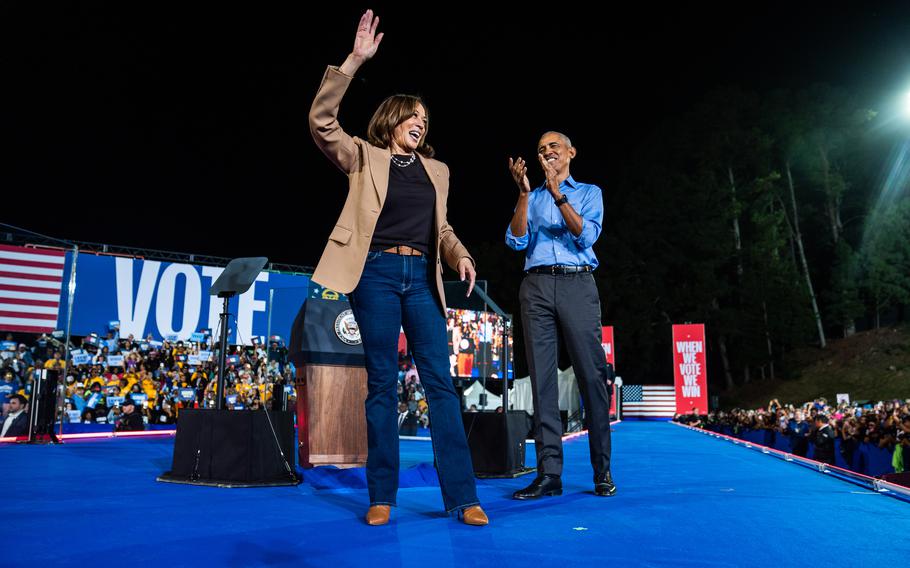 Kamala Harris stands on a stage and waves as she is applauded by Barack Obama.