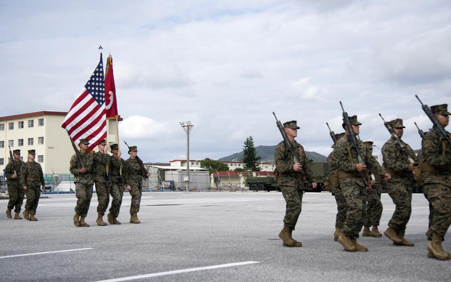 Marines hold an American flag and the unit’s colors as they march in formation at Camp Hansen.