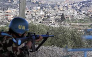 A soldier with a blue U.N. helmet aims a rifle from a vantage point overlooking a town.