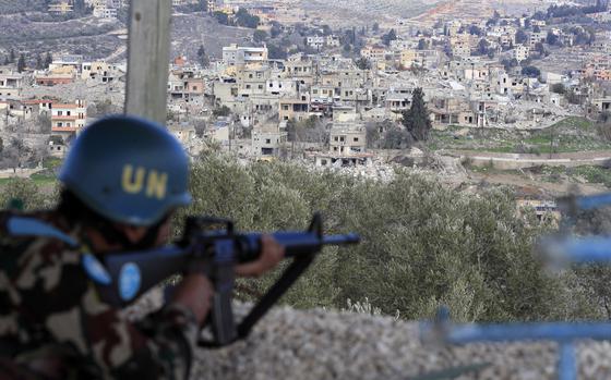 A soldier with a blue U.N. helmet aims a rifle from a vantage point overlooking a town.