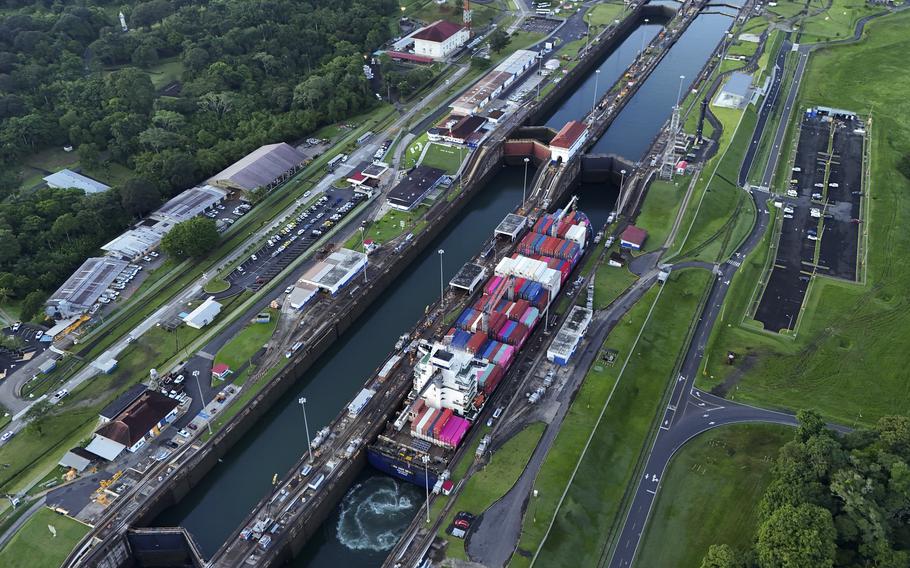 A cargo ship is seen from above passing through a narrow canal.