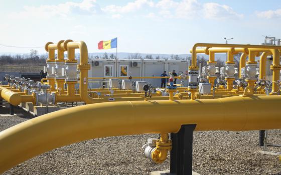 An array of yellow pipelines are seen with two men and a Moldovan flag in the background.