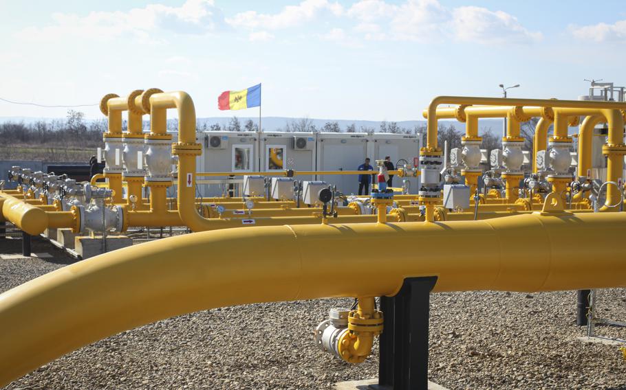 An array of yellow pipelines are seen with two men and a Moldovan flag in the background.