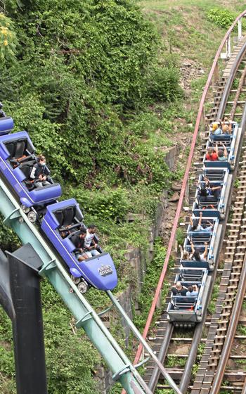 The Phantom’s Revenge goes downhill while the Thunderbolt makes its way uphill on National Roller Coaster Day on Aug. 16, 2020, at Kennywood Park in West Mifflin, Pa. The purple smooth-steel spine of Phantom’s Revenge interweaves with the track of the old-fashioned Thunderbolt wooden coaster. 